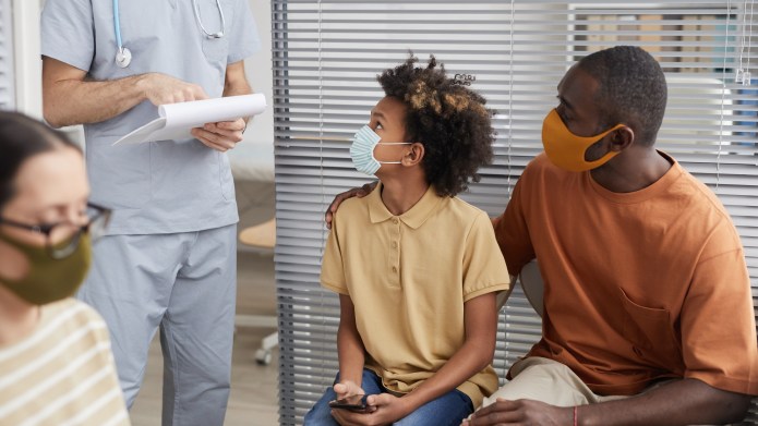 Portrait of African-American family wearing masks and looking at doctor while waiting in line at medical clinic